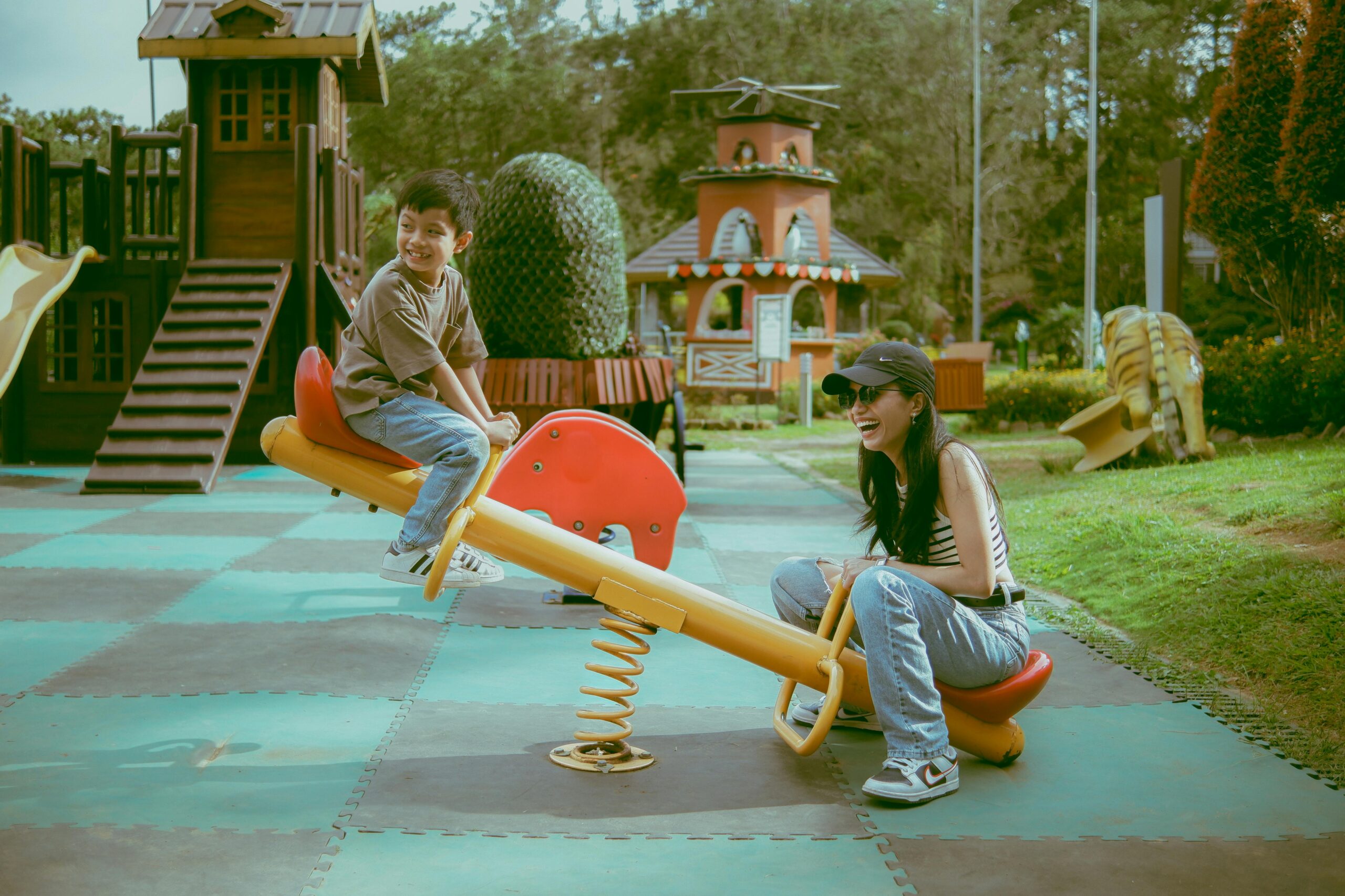 A mother and son laughing and playing on a seesaw in an outdoor playground.